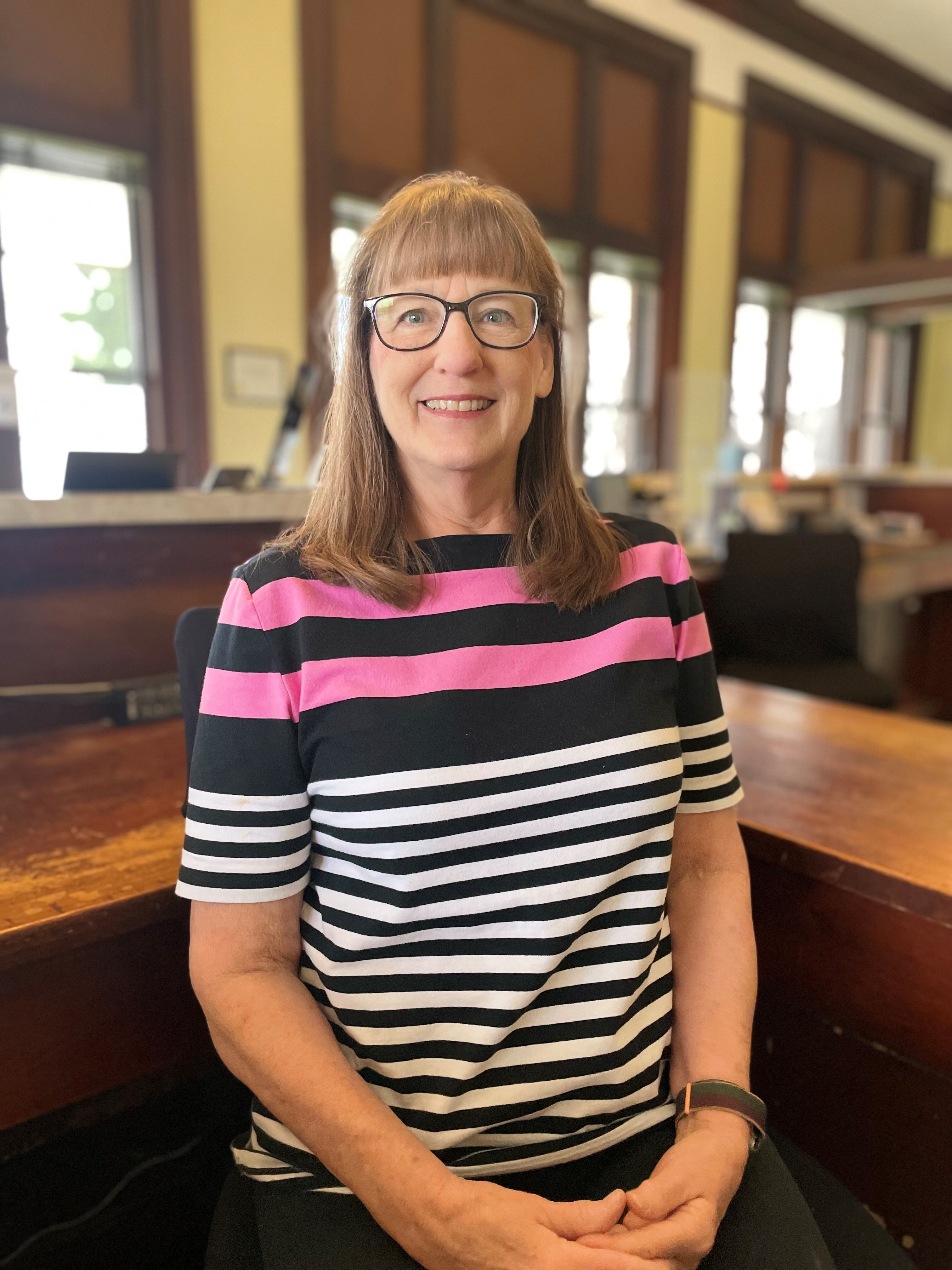 Female with glasses wearing a pink, white and black striped top